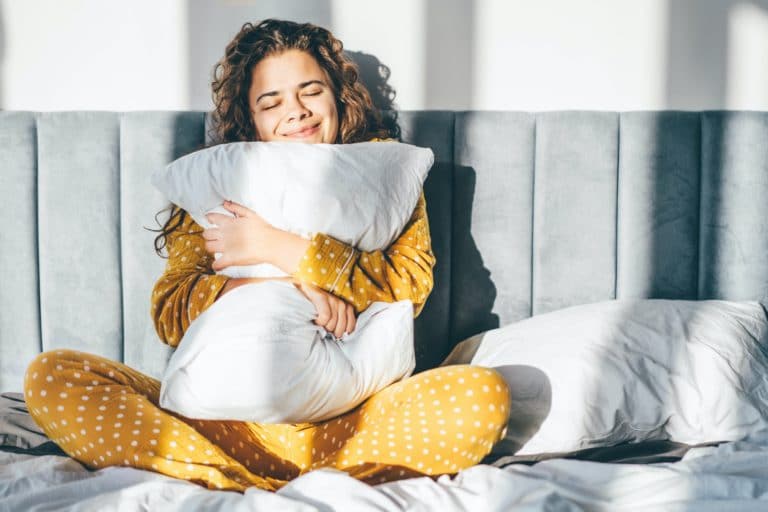 Woman in yellow pajamas hugging pillow and smiling.